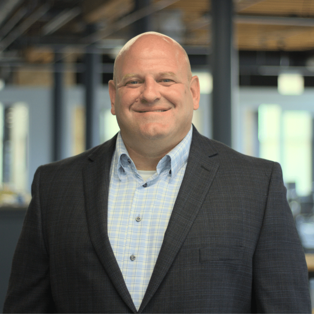 Matt Uhl, a Florida M&A Business Broker, stands facing the camera wearing a suit. Behind him an office background is blurred out.